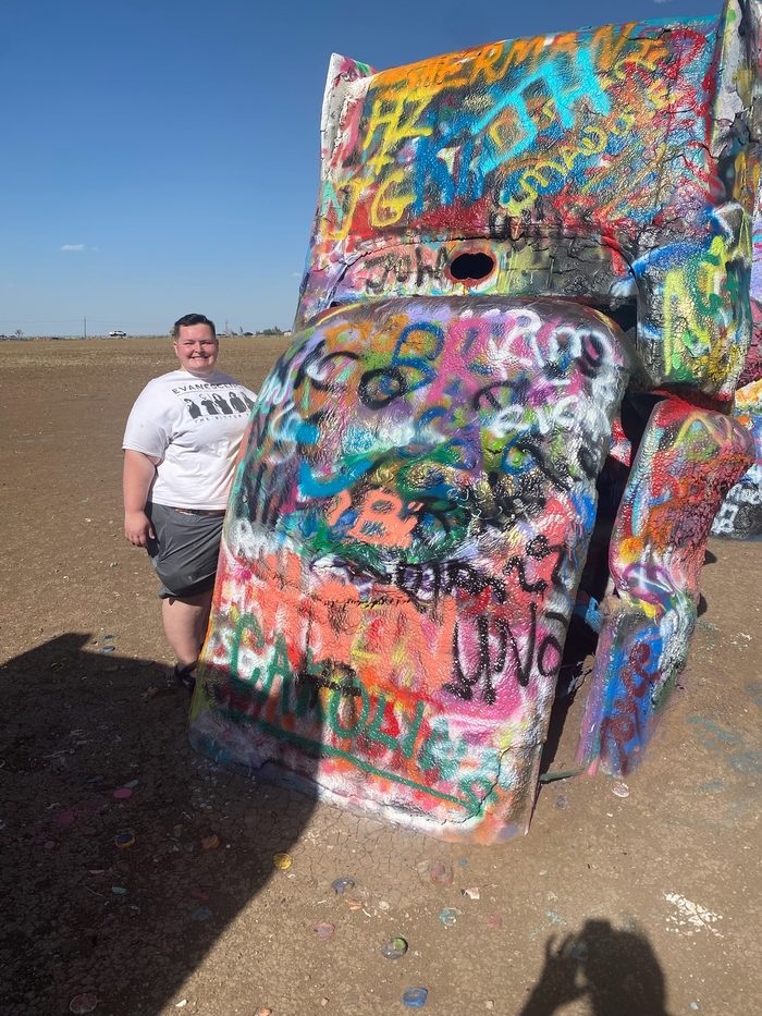 Amanda beside a spray-painted car buried nose-down at Cadillac Ranch.