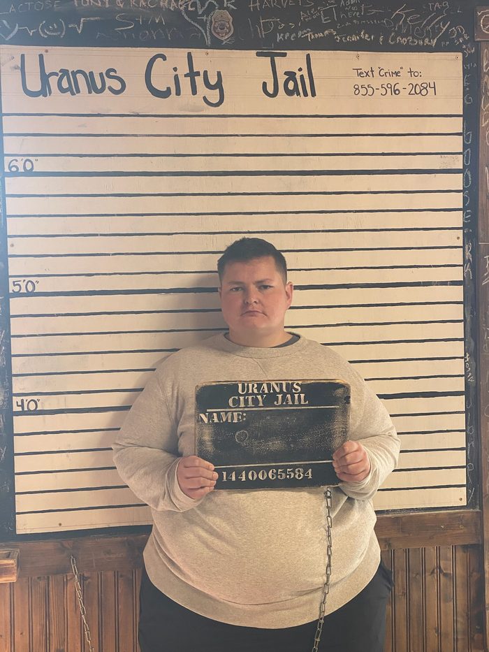 Amanda holding a novelty booking board against a height chart at the Uranus City Jail attraction.