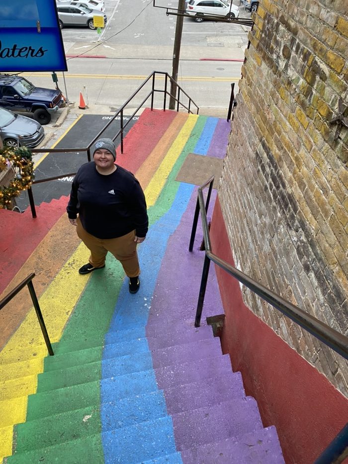 Amanda at the bottom of a flight of rainbow-painted alley steps.