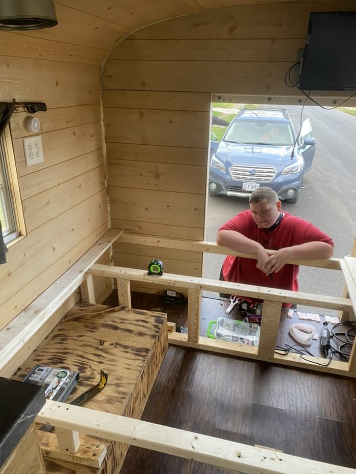 Amanda framing bench seating inside the bus, cedar walls half finished.