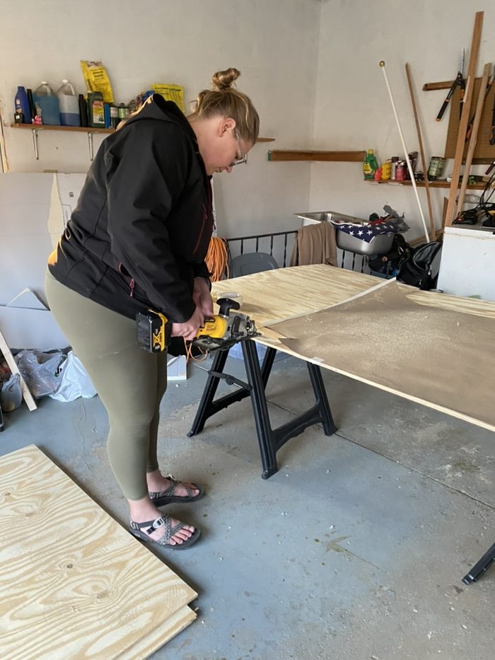 Robyn cutting a sheet of plywood with a circular saw in a garage.