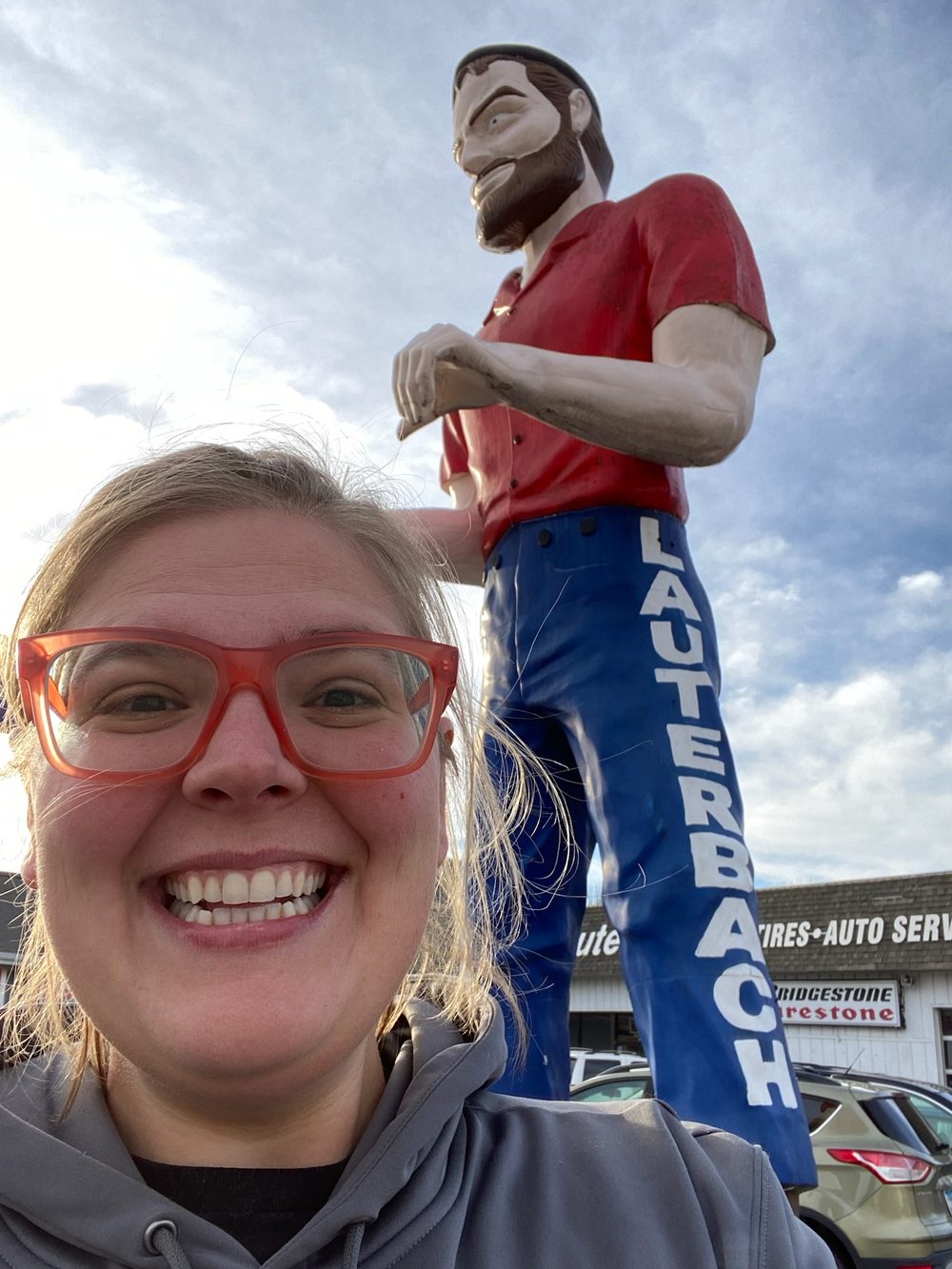 Robyn grinning in front of a roadside fiberglass lumberjack statue.