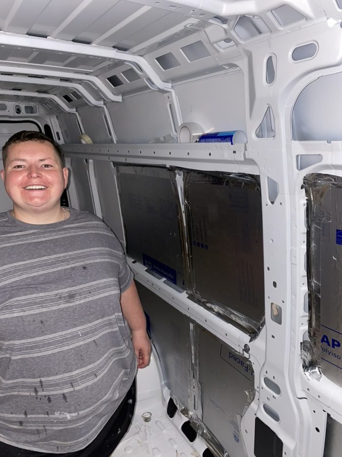 Amanda inside an empty white van shell part-way through insulating it.
